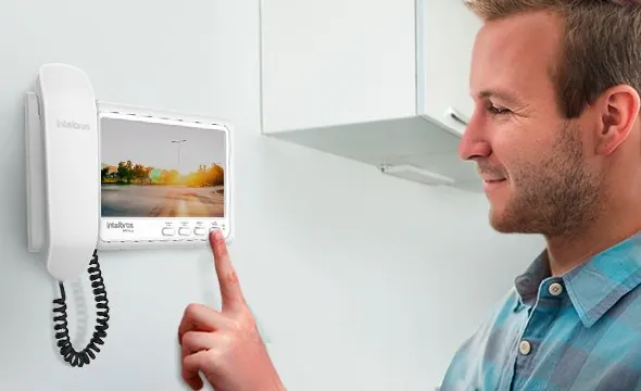 Homem atendendo um vídeo porteiro Intelbras com tela colorida na parede